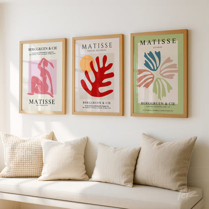 collection of three framed modern art pieces by Matisse in light wood frames displayed on a light wall alongside cushions on a sofa