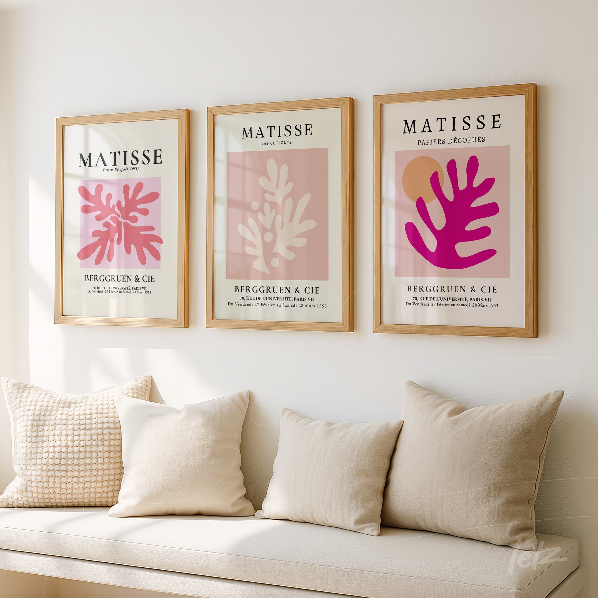 composition of three framed artworks in beige frames featuring abstract designs in shades of pink and red displayed on a light wall with neutral cushions on a fabric sofa