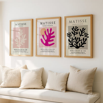 composition of three modern wall art pieces with light wood frames showcasing botanical designs in pink and black