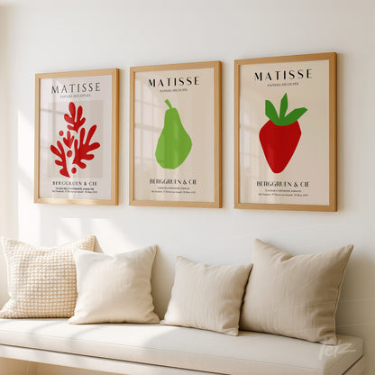 composition of three framed wall art pieces featuring modern style illustrations of a red coral, a green pear, and a red strawberry, all in light wood frames with a neutral background