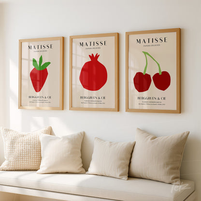 series of decorative wall art featuring red fruit illustrations in light wood frames on neutral wall