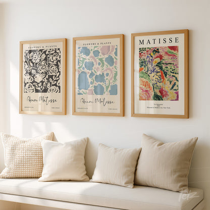 collection of three framed artworks in light wood, displayed on a neutral wall, featuring flower and plant illustrations in the style of Henri Matisse