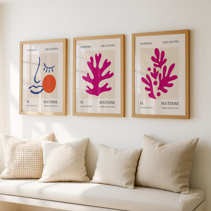 collection of three framed artworks featuring abstract illustrations in shades of pink and orange with neutral backgrounds and cream-colored cushions on a sofa