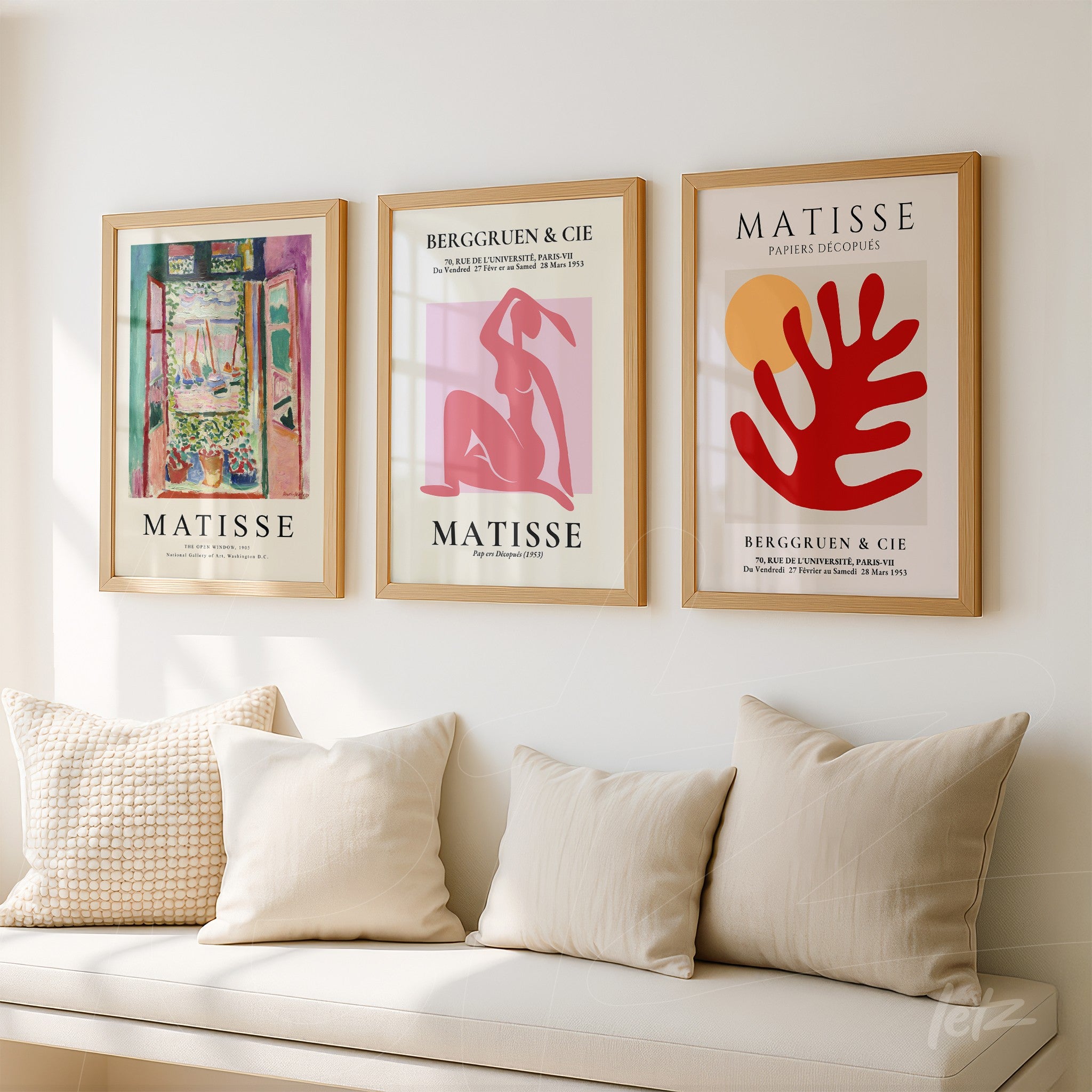 composition of three framed artworks by matisse in light wood frames displayed on a white wall with cream pillows on a sofa in the background