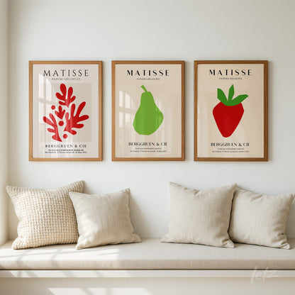 composition of three framed wall art pieces featuring simple illustrations of fruits and vegetation in light wood frames displayed above a neutral sofa