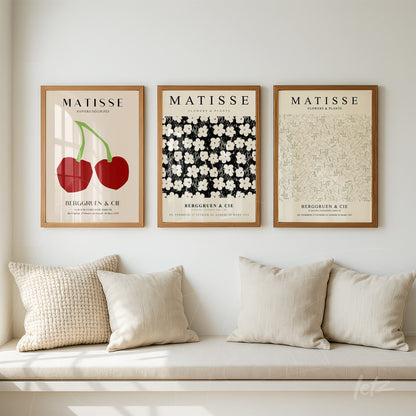 collection of three framed artworks inspired by Matisse, featuring red cherries, white flowers on black background, and light green floral pattern in light wood frame