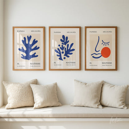 set of three framed artworks showcasing abstract organic shapes in blue and red on neutral background with light wood frames