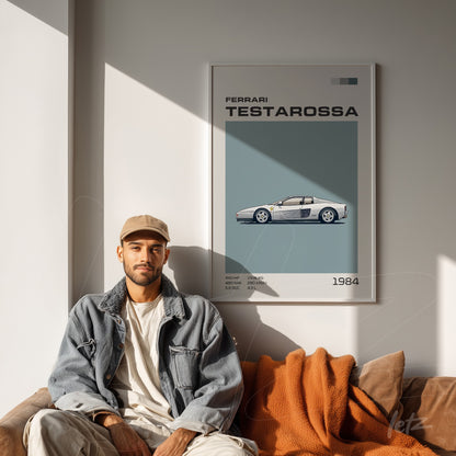 framed wall art featuring a Ferrari Testarossa illustration displayed on a light wall with a man sitting beside it