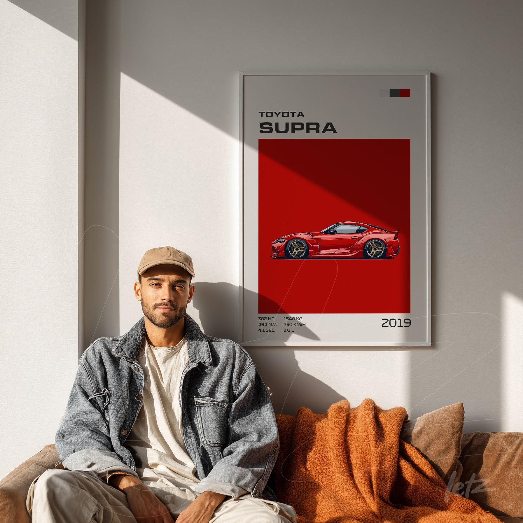 framed illustration of the toyota supra car on a red wall with shadow, featuring a model sitting next to it on a brown sofa