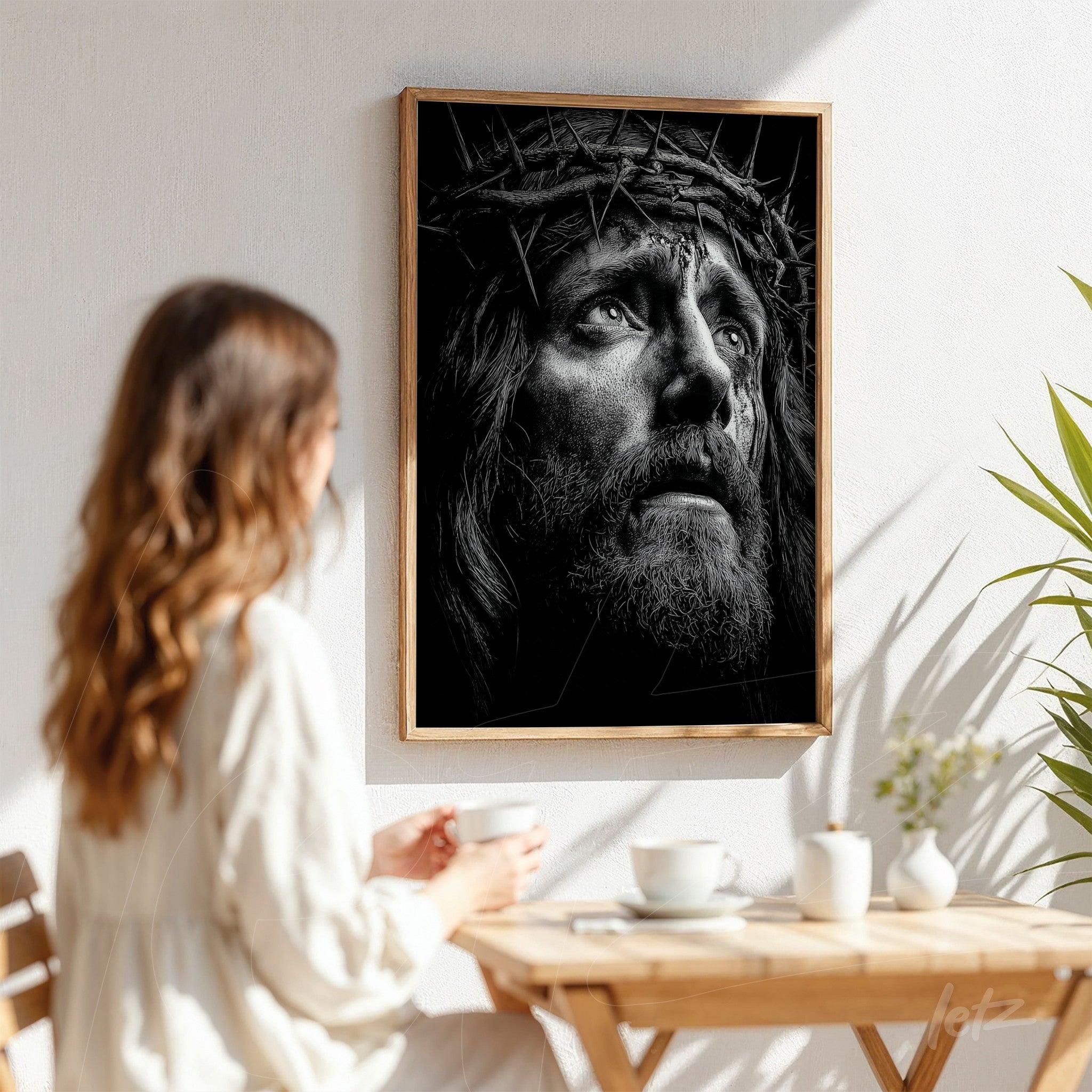 black and white portrait of Jesus with crown of thorns in light wood frame displayed on white wall next to a plant