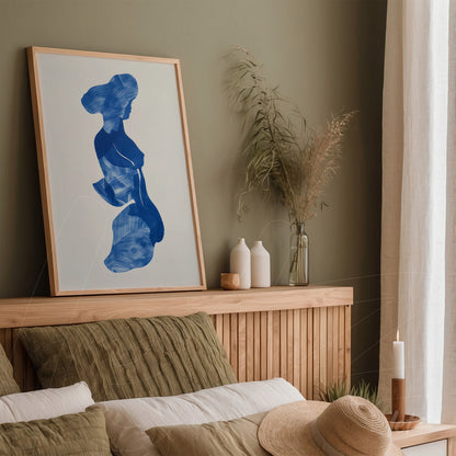 framed artwork with abstract blue design displayed above a wooden headboard in a minimalist decor setting