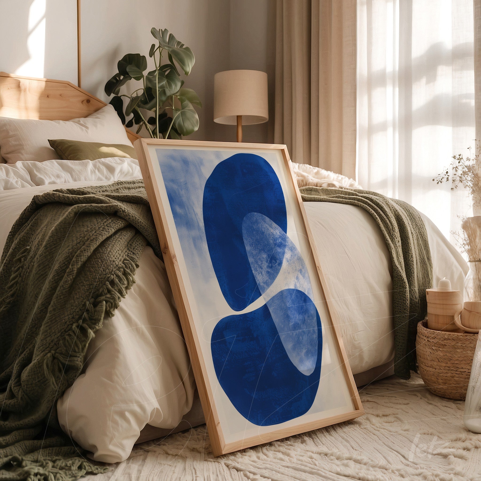 framed artwork with abstract blue shapes on light background leaning beside a bed in a cozy setting