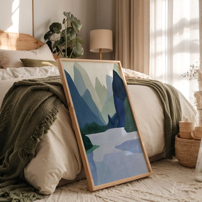 framed artwork featuring abstract mountains in shades of green and blue leaning beside a bed in softly lit bedroom