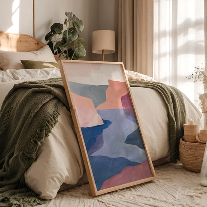 framed contemporary art featuring an abstract landscape in shades of pink, blue, and beige leaning next to a cozy bed in a warm bedroom