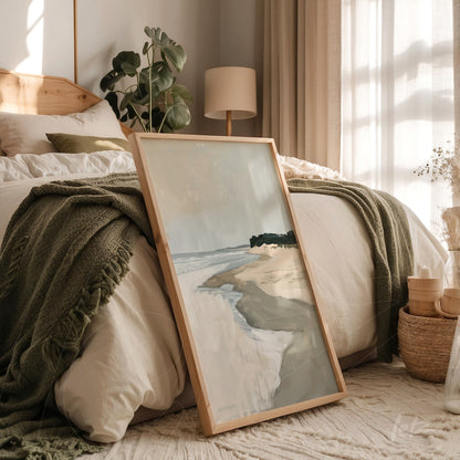 framed art of abstract beach scene in light wood frame, leaning next to bed with green blanket