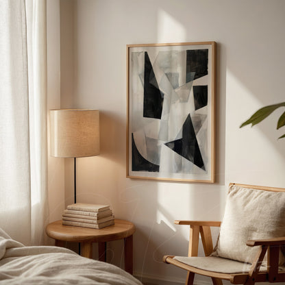 abstract artwork featuring geometric shapes in black and gray tones in a light wooden frame displayed in a well-lit setting next to a table lamp