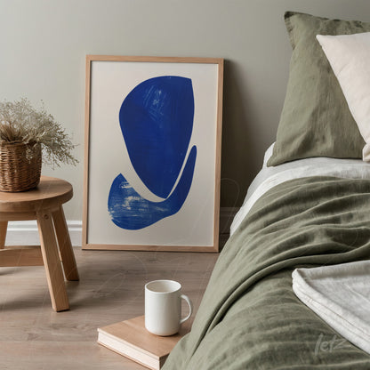 framed wall art featuring abstract design in blue, positioned next to a bed with green and beige bedding