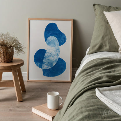 framed abstract blue art displayed on a wooden side table next to a bed