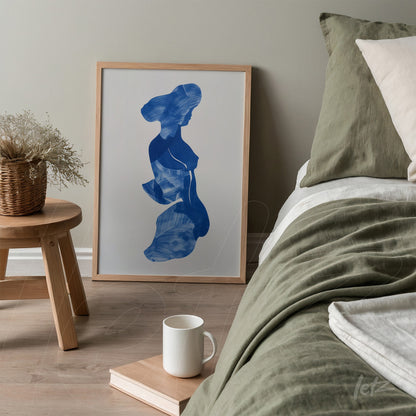 framed artwork featuring a blue silhouette of a woman next to a bed with neutral-toned bedding
