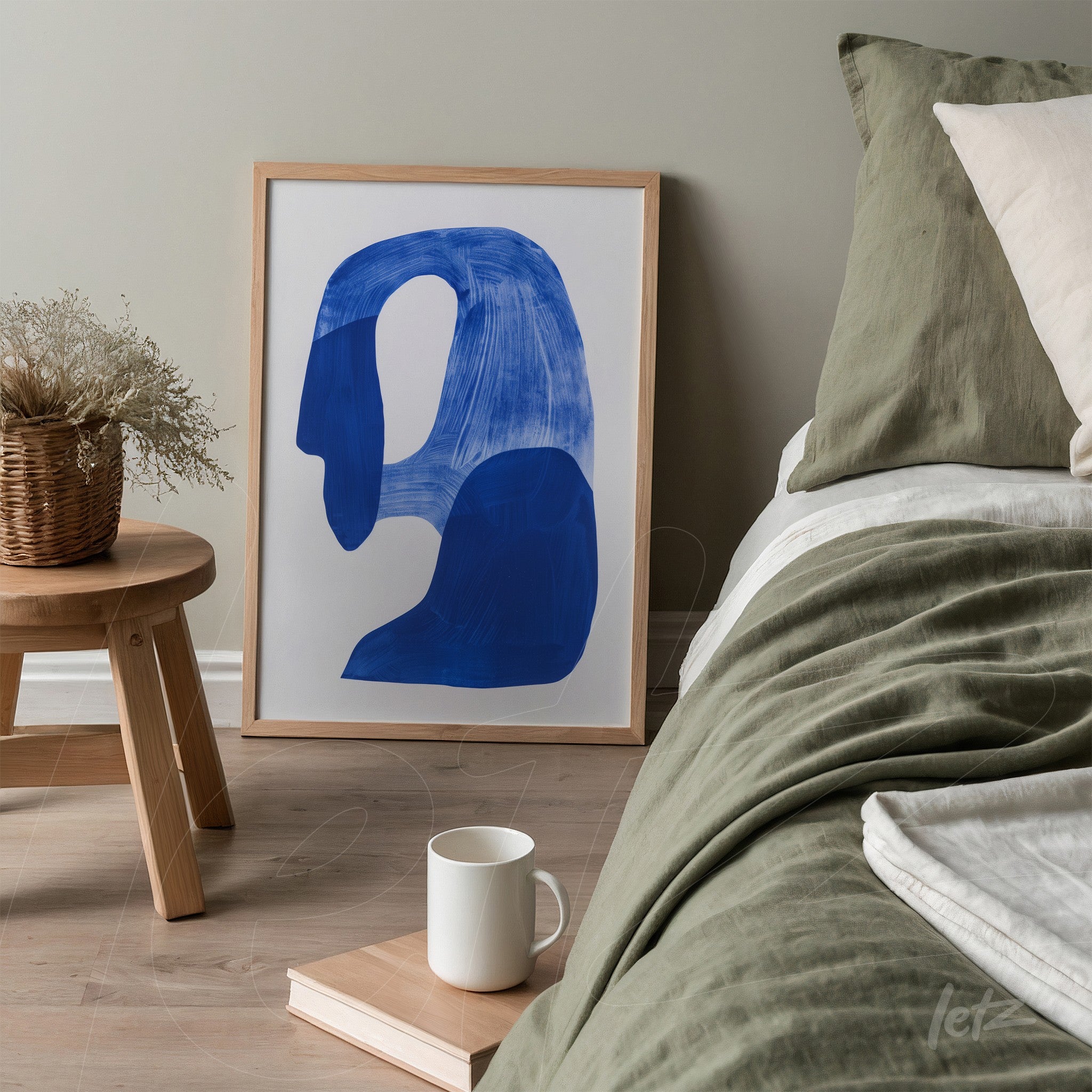 framed abstract art in dark blue shapes set next to a bed with a green coverlet