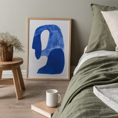 framed abstract art in dark blue shapes set next to a bed with a green coverlet