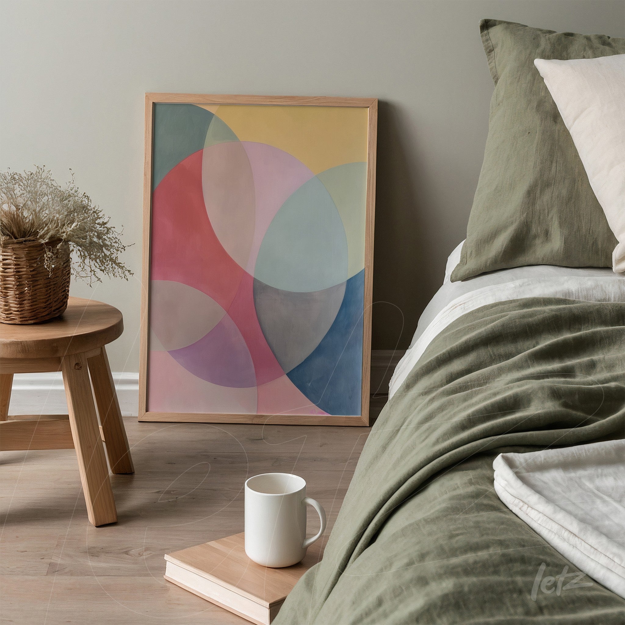 framed artwork with pastel geometric shapes leaning beside a bed with green bedding and light pillows