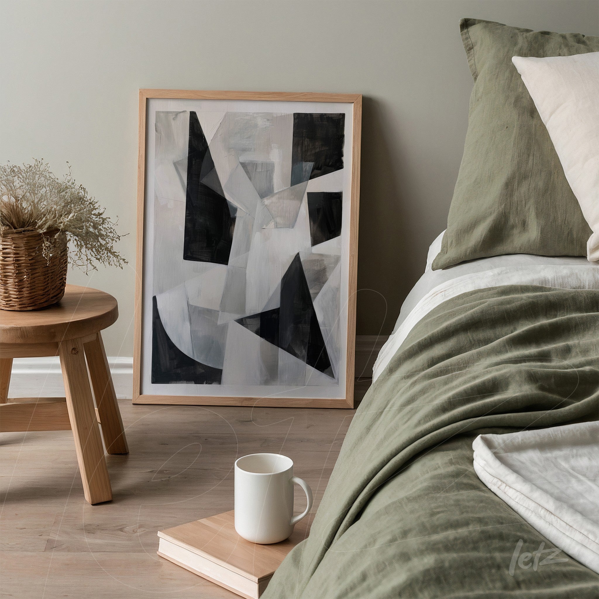 framed abstract artwork in black and white, light wood frame leaning beside bed with green bedding
