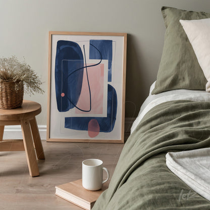 abstract art print in blue and pink tones in a light frame displayed next to a bed with green bedding