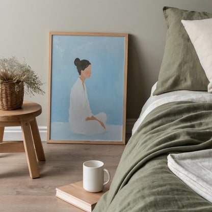 minimalist wall art depicting a seated woman against a light blue background in a light wooden frame leaning beside a bed