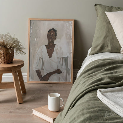 framed artwork featuring a neutral-toned portrait of a seated woman leaning against a bed in a chic setting