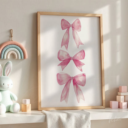 framed artwork featuring three pink watercolor bows, displayed in a bright room with natural wood frame