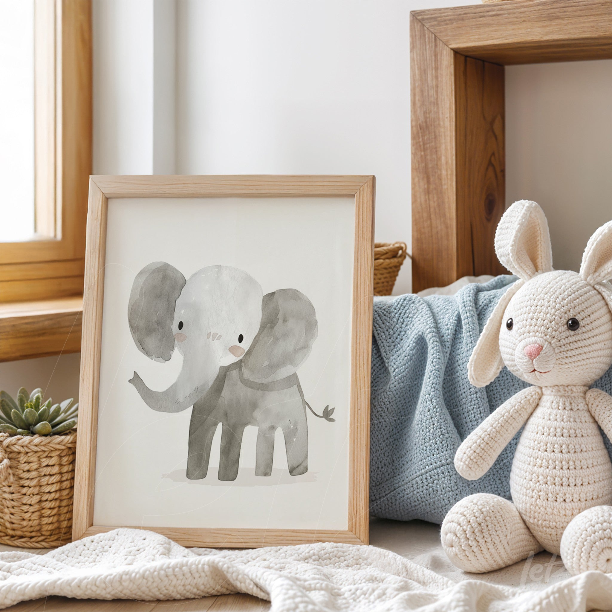 framed illustration of a stylized elephant in light wood frame displayed on a table with a rabbit toy and blue blanket