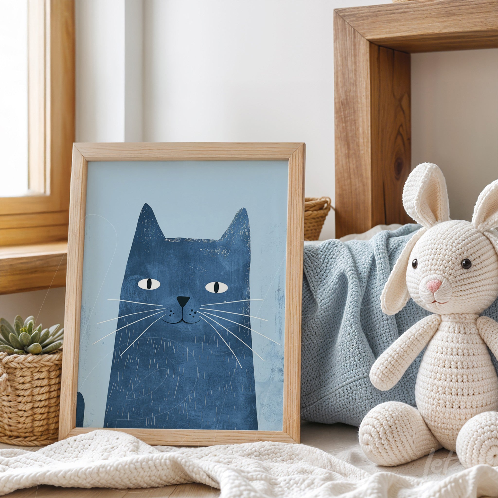 framed artwork of a blue cat illustration in a light wood frame, displayed on a couch with cushions and plush toys