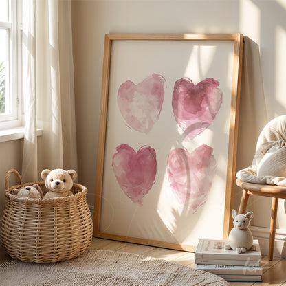 framed artwork with four pink hearts on white background in light wood frame displayed in a bright room next to a teddy bear in a basket