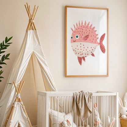 framed artwork of a pink pufferfish displayed in a nursery beside a crib and white play tent