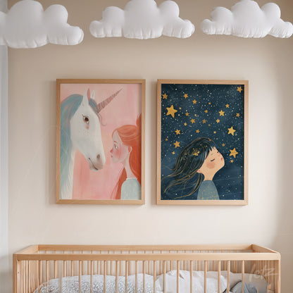 pair of decorative prints featuring whimsical illustrations, one depicting a girl with a unicorn against a pink background and the other showing a girl gazing at stars on a dark blue backdrop, both in light wood frames