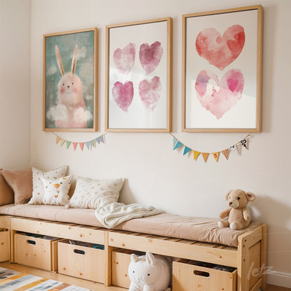 set of framed watercolor heart art in various shades of pink and a bunny illustration in light wood frames displayed on a light wall