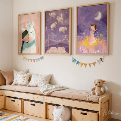 collection of three children's framed artworks featuring a unicorn, sheep in a dreamy landscape, and a girl surrounded by flowers in light wood frames displayed over a wooden bench in a cozy setting