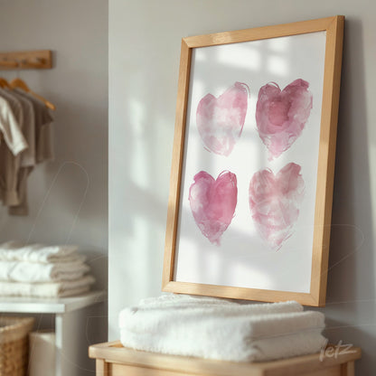 framed artwork of four watercolor hearts in shades of pink with a light wood frame