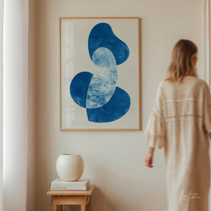 modern wall art featuring abstract shapes in blue framed in light wood on a neutral wall