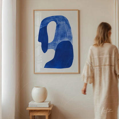 abstract wall art in light frame featuring blue shapes on white background displayed on light wall next to a vase
