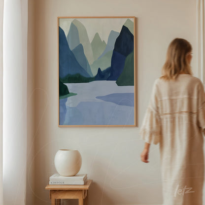 framed artwork depicting a mountainous landscape in shades of blue and green, displayed on a light wall