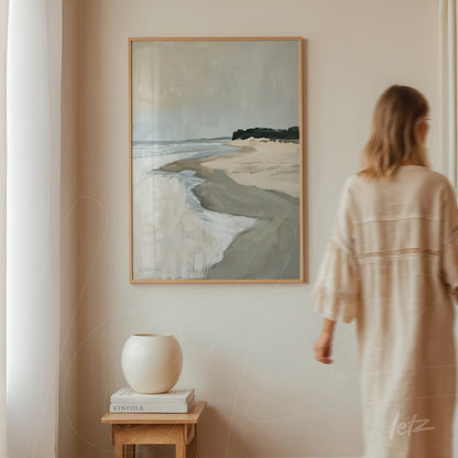 framed artwork depicting a beach landscape on a neutral wall beside a person walking by