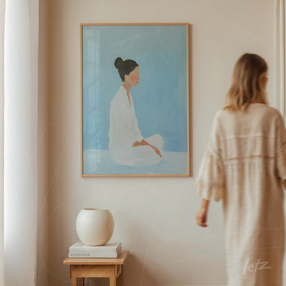 framed minimalist art depicting a seated woman against a light blue background with light wood frame displayed in a neutral wall setting