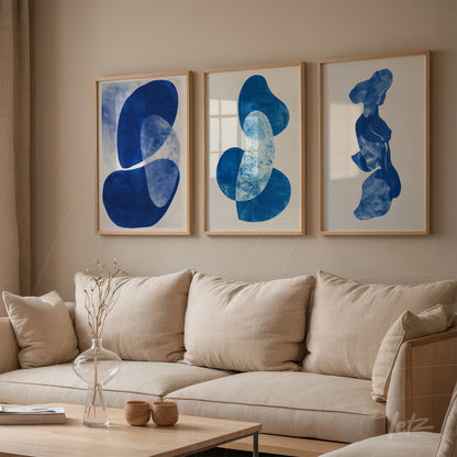 set of three framed artworks featuring abstract blue shapes with light wood frames displayed on a neutral wall in a cozy setting