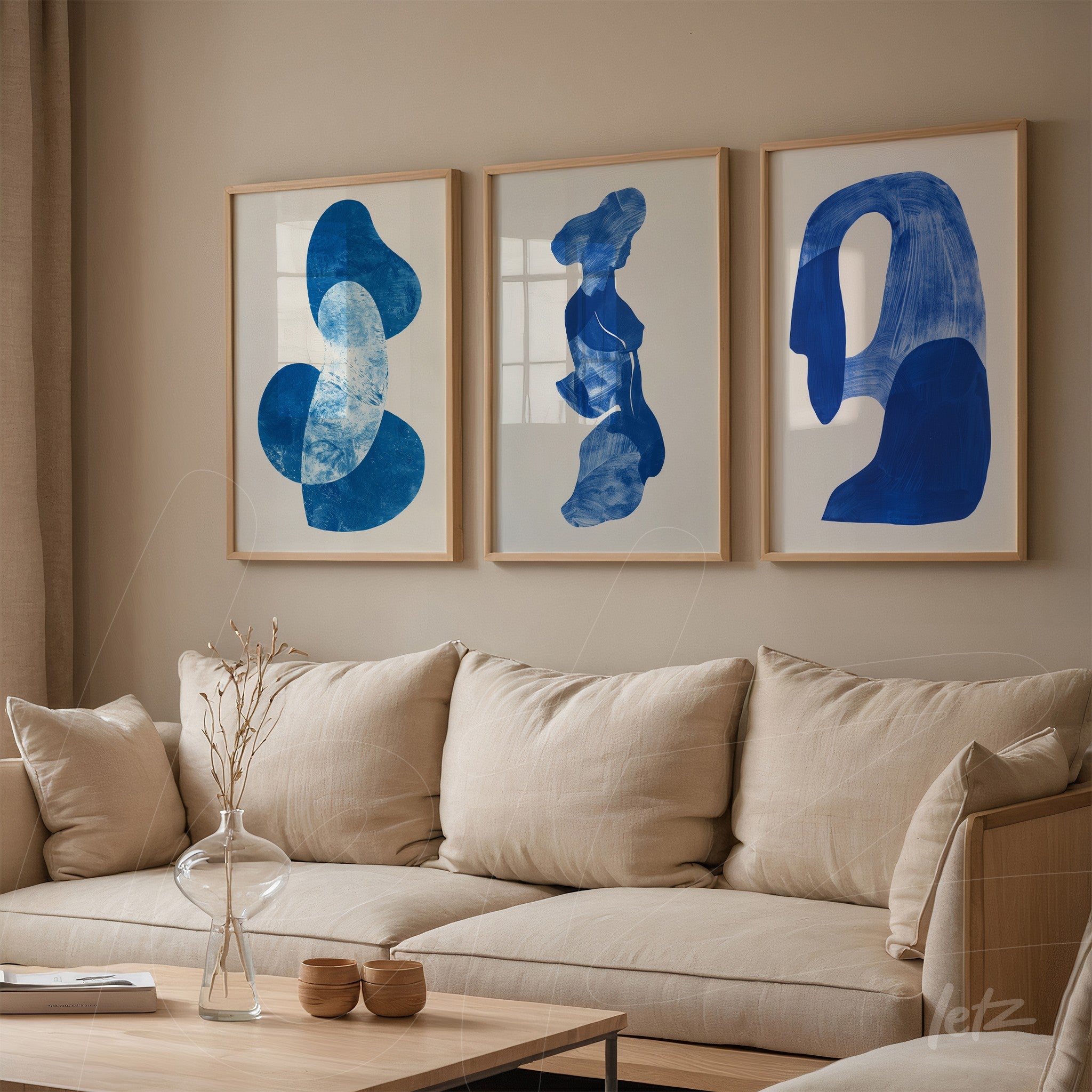 set of three framed artworks featuring abstract blue shapes displayed on a neutral wall beside a cozy sofa