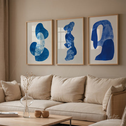 set of three framed artworks featuring abstract blue shapes displayed on a neutral wall beside a cozy sofa