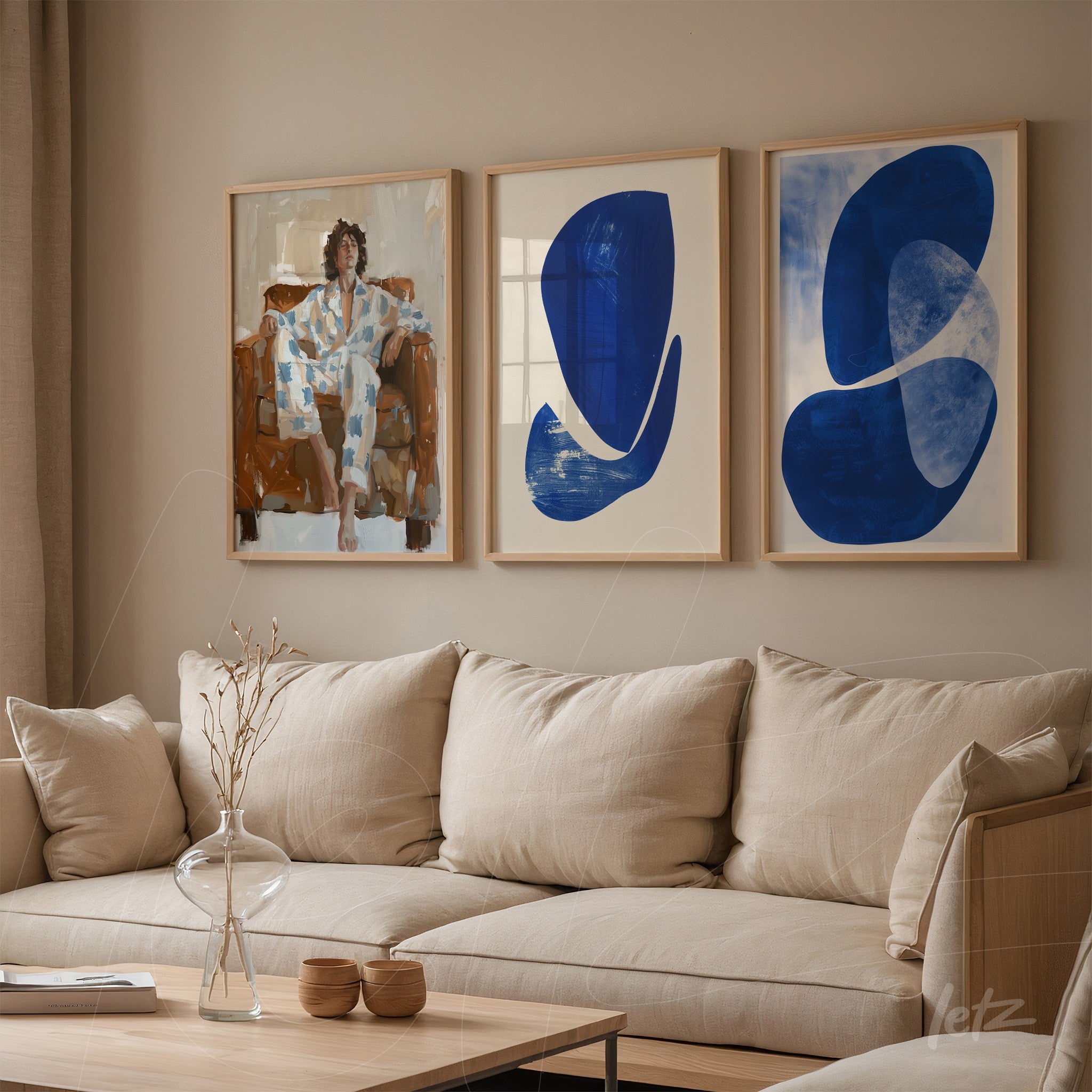 composition of three framed artworks in wooden frames featuring abstract designs in shades of blue and a human figure sitting on a light fabric sofa against a beige wall