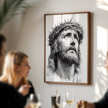framed artwork depicting the face of Christ with a crown of thorns displayed on a light wall with people in a social setting in the background