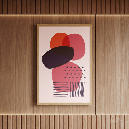 poster featuring geometric art with overlapping shapes in pink and orange hues, displayed in a gold frame on a textured wooden wall